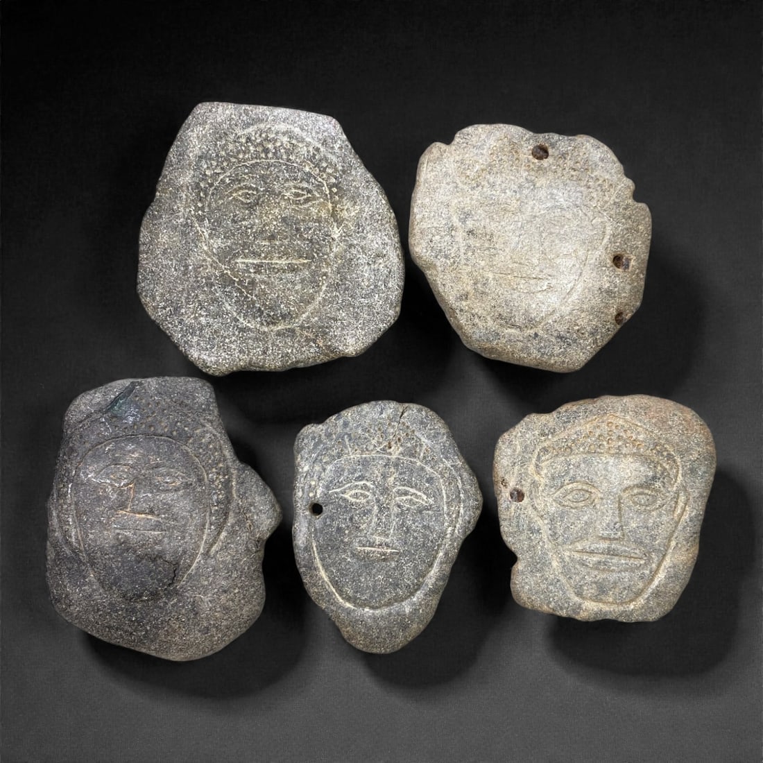 A Sino-Siberian Stone Anthropomorphic Plaque Group, Late 1st Millennium BCE, 87W: Carved from dense stone of varying tones, the group comprises five anthropomorphic plaques, each worked in low relief with schematic human features. The figures are rendered frontally, with simplified