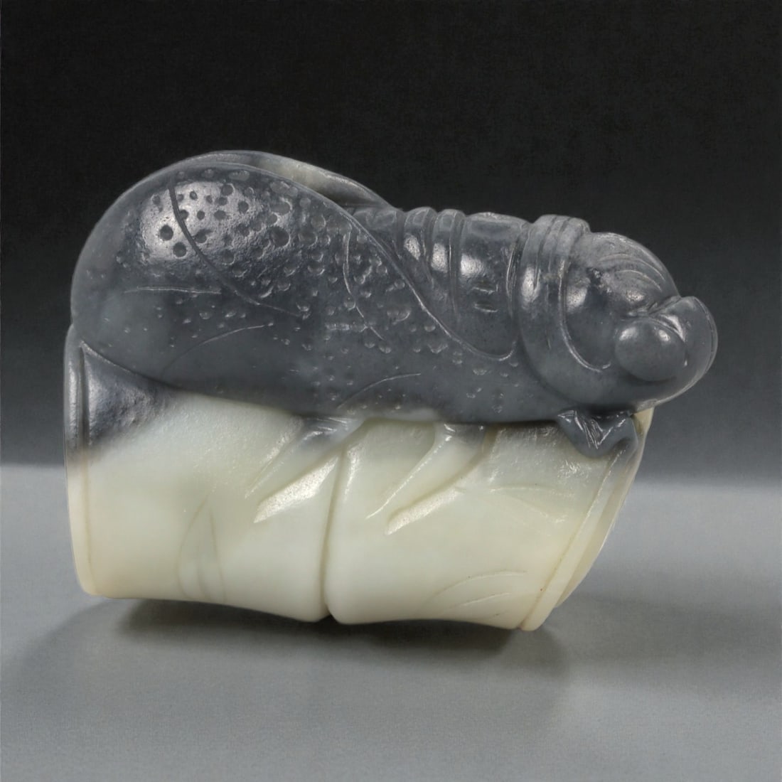 A Chinese Jade Mantis on Bamboo Ornament, 20th Century, 16FB: Carved from bi-colored jade with a creamy white lower section and a darker grey upper layer, the ornament is worked in the round as a praying mantis resting atop a section of bamboo. The mantis is ren