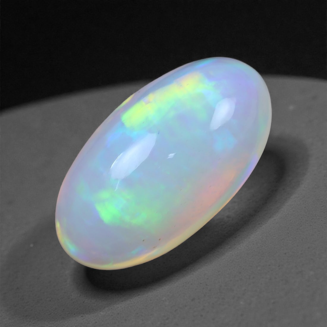 5.88 Carats Oval Cabochon Opal - Natural Ethiopian Stone 14.7x8.1x7.3mm, 49XH: This vivid Welo opal captivates with glowing ribbons of lime green, icy violet, and flashes of pastel blue cascading across its translucent body. The gem's high-domed oval silhouette maximizes light i