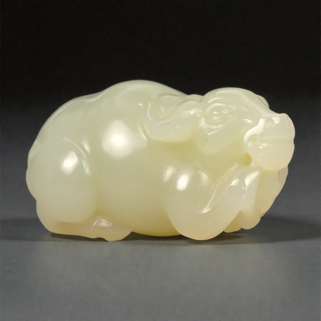 A Chinese Jade Buffalo Carving, 20th Century, 88FA: Carved from pale yellow jade with a creamy, semi-translucent appearance and subtle tonal variation, the object represents a buffalo shown recumbent with the legs folded beneath the body. The animal is