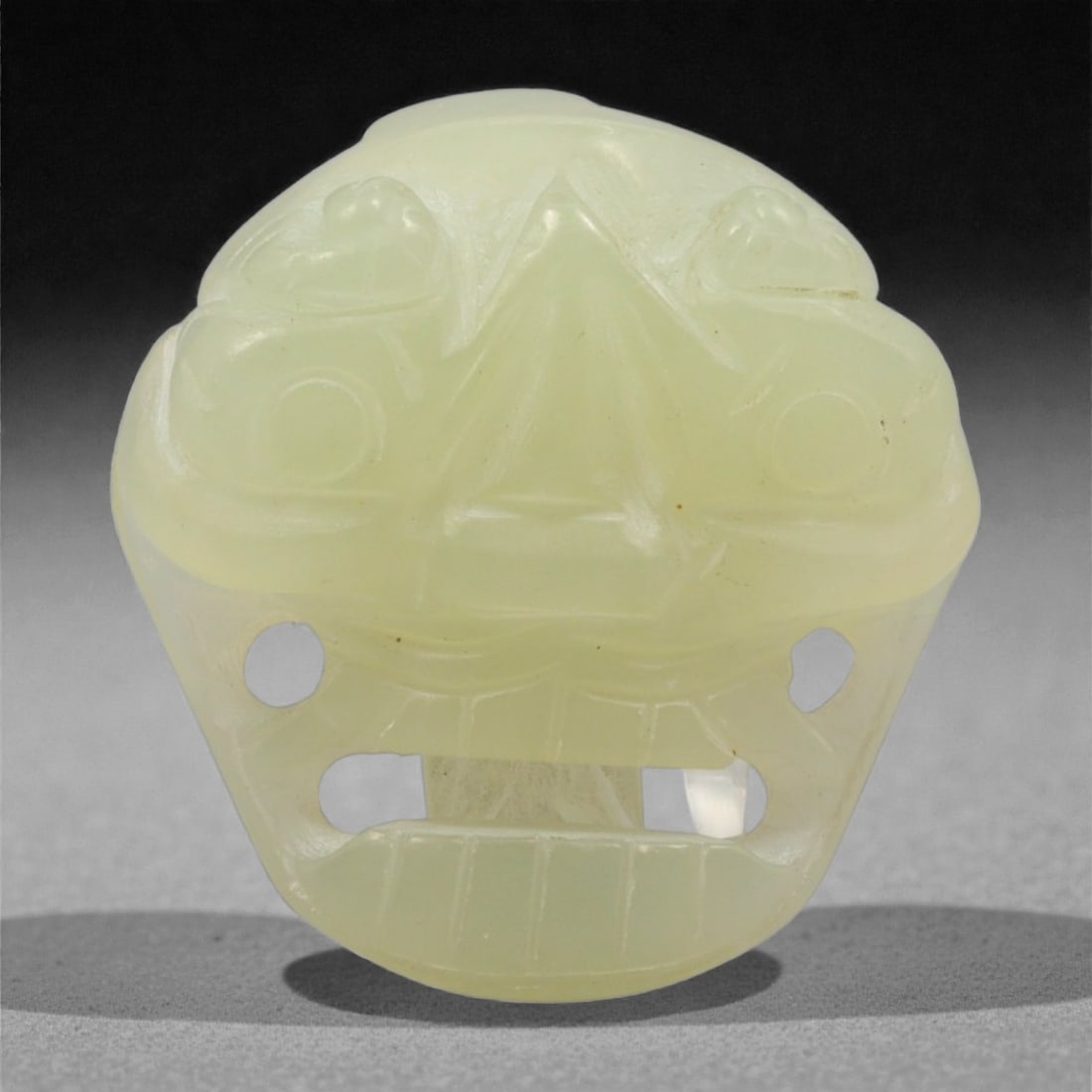 A Chinese Jade Belt Buckle with Beast Mask, 20th Century, 40YC: The buckle is carved from pale celadon jade with a soft, even translucency and minor natural inclusions. It is formed as a compact plaque with rounded contours, the front carved in shallow relief with