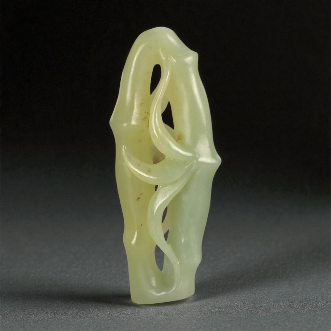 A Chinese Nephrite Jade Bamboo-Form Carving, 20th Century, 66FA: Carved from pale green nephrite jade with areas of translucency and scattered natural inclusions, the object is modeled as a stylized section of bamboo. The elongated vertical form is articulated with