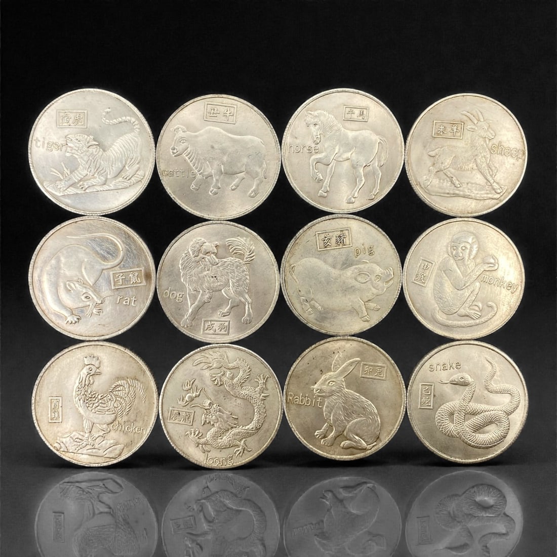 A Chinese Twelve Zodiac Commemorative Coin Set, 20th Century, 97FH: The group comprises twelve circular commemorative coins, each struck in a silver-colored metal alloy and decorated in relief with one of the animals of the Chinese zodiac, including rat, ox, tiger, ra