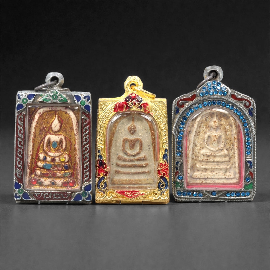 A Group of Thai Clay and Composite Buddhist Amulets, 20th Century, 15ZG: Comprising three molded Buddhist amulets formed from pale buff and light brown clay compositions, each depicting a seated Buddha in meditation posture upon a stepped base. The figures are rendered in