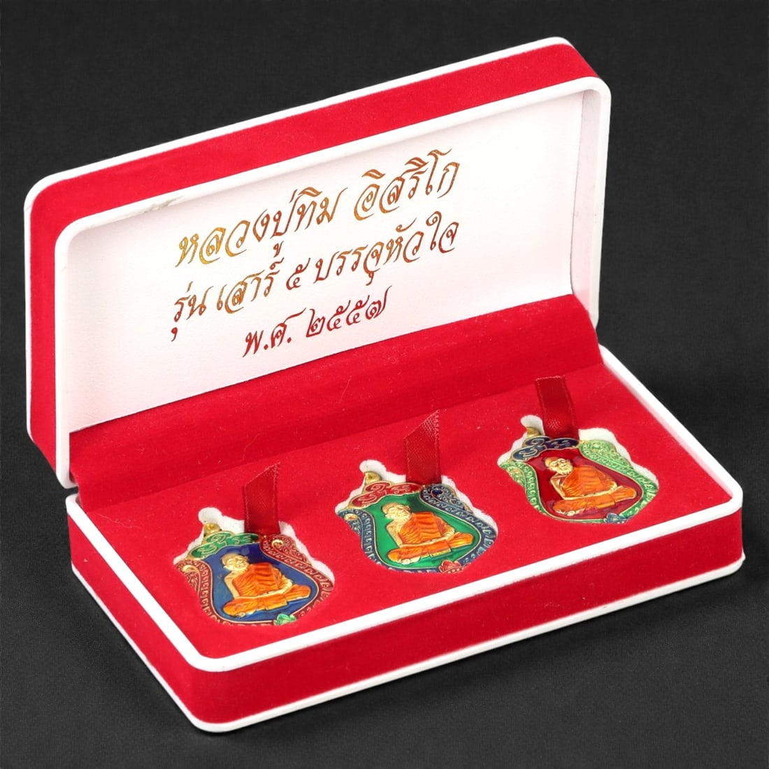 A Thai Enamel and Bronze Seated Monk Amulet Set, Late 20th Century, 54FJ: The set comprises three shield-shaped amulets cast in bronze and finished with polychrome enamel, each depicting a seated Buddhist monk shown frontally in meditative posture. The figure is rendered in