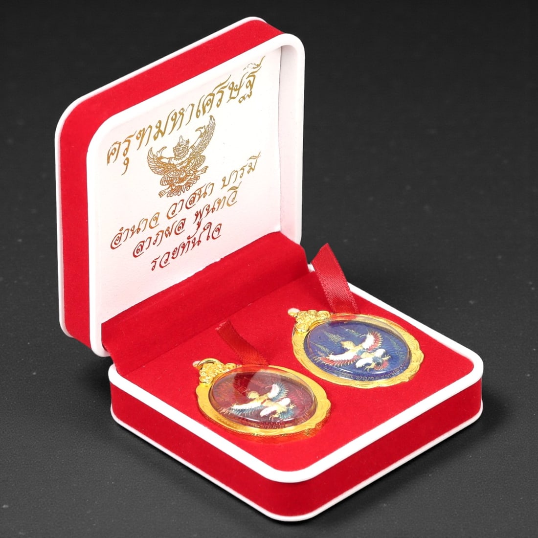 A Thai Gilt Bronze and Enamel Garuda Medallion Set, Late 20th Century, 25FJ: The set comprises two circular medallions cast in bronze and finished with gilt mounts and polychrome enamel, each depicting the Garuda shown with wings outstretched in frontal orientation. The mythol