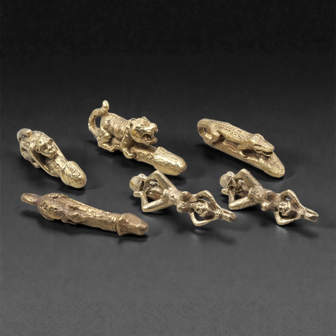 A Group of Thai Copper Alloy Erotic and Phallic Amulets, 20th Century, 3ZG: Cast in copper alloy with worn gilt-toned surfaces and areas of darker patination, the group comprises a selection of small-scale erotic and phallic amulets associated with Thai folk and esoteric trad