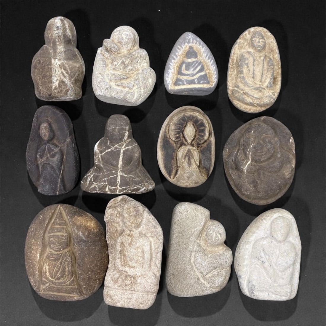 A Group of Japanese Stone Buddhist Figures, Edo Period, 89Z: Carved from light to dark-toned stone with natural veining, inclusions, and areas of surface wear, the group comprises twelve small Buddhist devotional figures of irregular, rounded, and pebble-like f