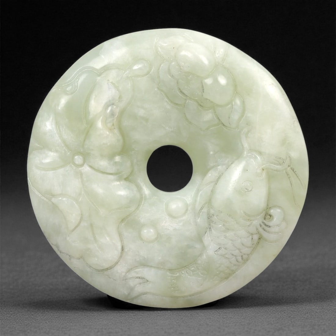 A Chinese Hetian Jade Bi Disc with Fish Decoration, 20th Century, 78FH: Carved from pale celadon Hetian nephrite jade with a semi-translucent body and subtle cloudy inclusions, the disc is formed with a central circular aperture and a flattened profile. One face is worked