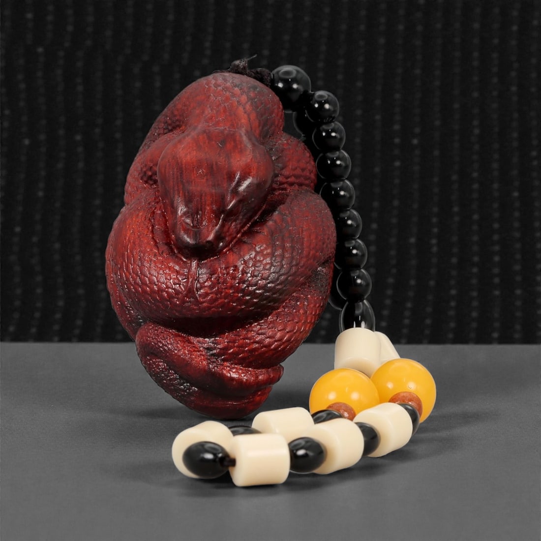 A Chinese Wood Snake Figure, 20th Century, 80FD: Carved from dark reddish-brown wood with a polished surface, the figure represents a coiled snake rendered in compact form. The body is tightly wrapped in overlapping loops, with the head emerging at