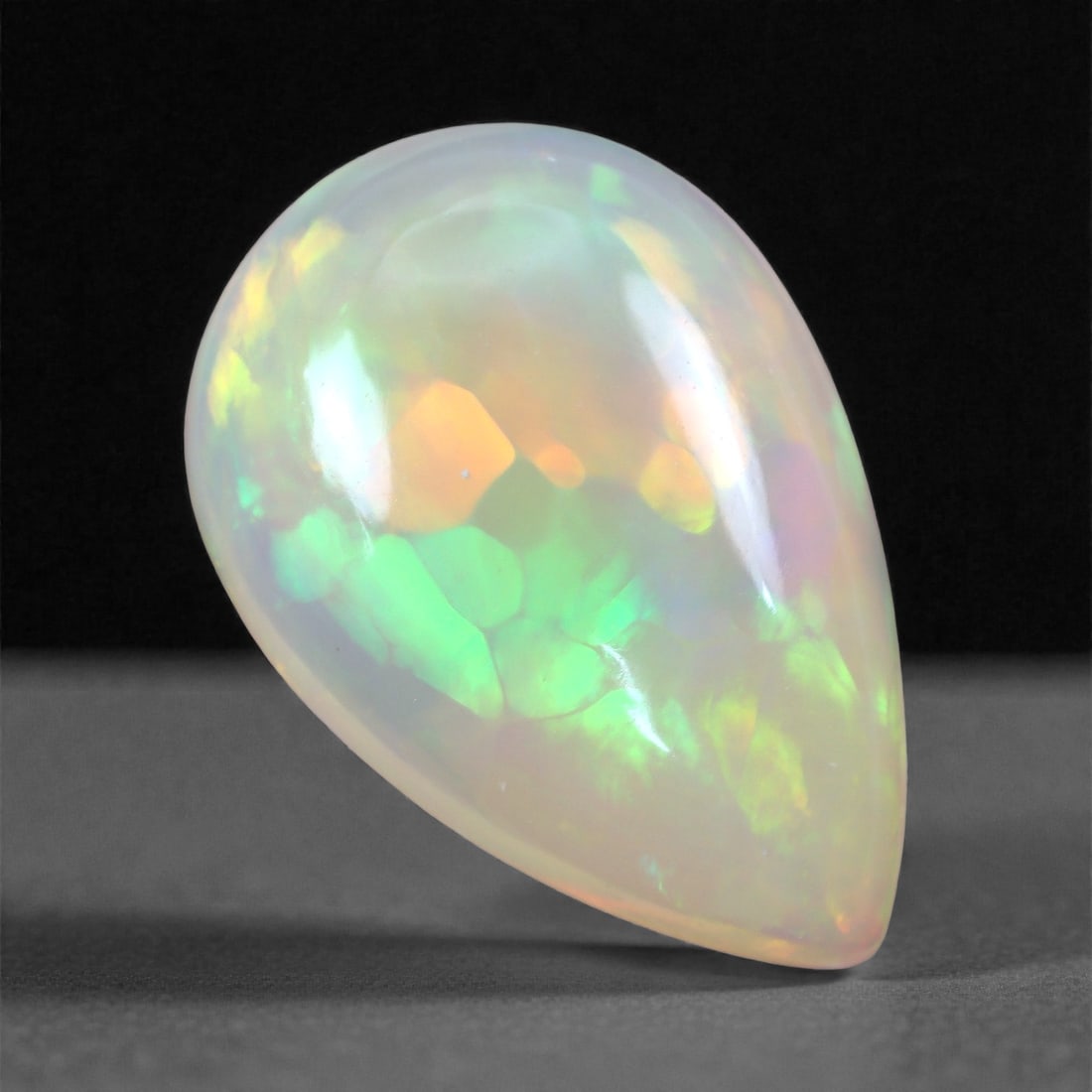 6.06 Carats Mosaic Fire Welo Opal - Ethiopian Pear Cabochon 17.4x11.6x5.4mm, 8XH: This striking 6.06 carat Welo opal features an electrifying mosaic pattern of angular play-of-color-vivid emerald greens, glowing tangerine oranges, and subtle violets dance beneath its glossy pear ca