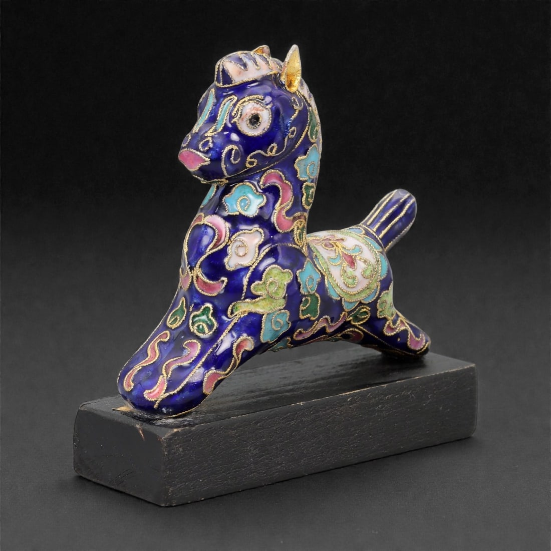 A Chinese Cloisonne Enamel Horse Effigy on Wooden Stand, 20th Century, 94FG: Modeled as a dynamic horse shown in a leaping or extended stride posture, the effigy is constructed over a metal core and decorated overall in cloisonne enamel on a deep cobalt blue ground, the surfac