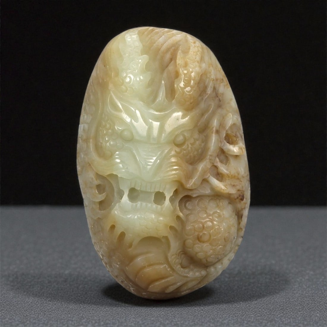 A Chinese Nephrite Jade Dragon Pendant, 20th Century, 56FB: Carved from pale celadon Hetian nephrite jade with areas of warm russet veining and natural inclusions, the pendant is of elongated oval form and worked in high relief on one face. The composition dep