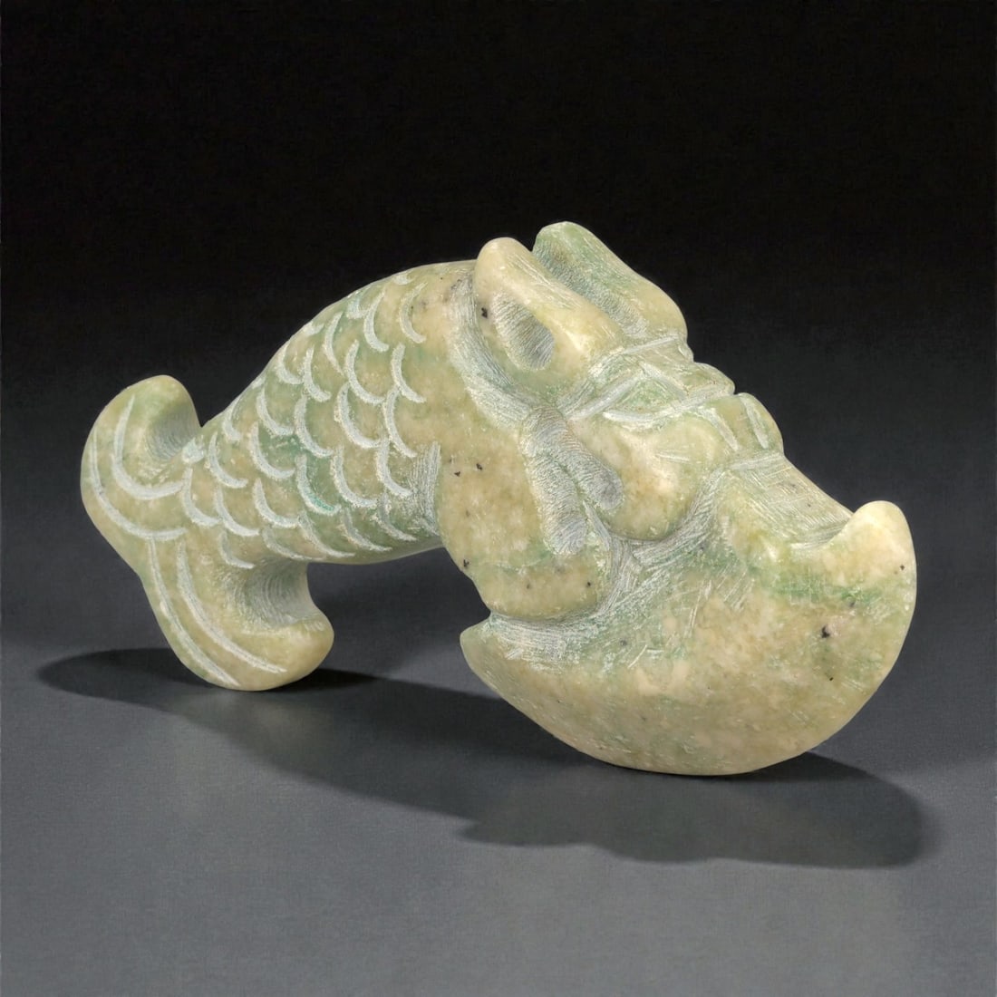 A Chinese Hardstone Fish-Form Axe, 20th Century, 32YB: Carved from mottled pale green and buff-toned hardstone with scattered dark inclusions, the object is worked in the stylized form of a fish combined with an axe blade profile. The head is broadened an