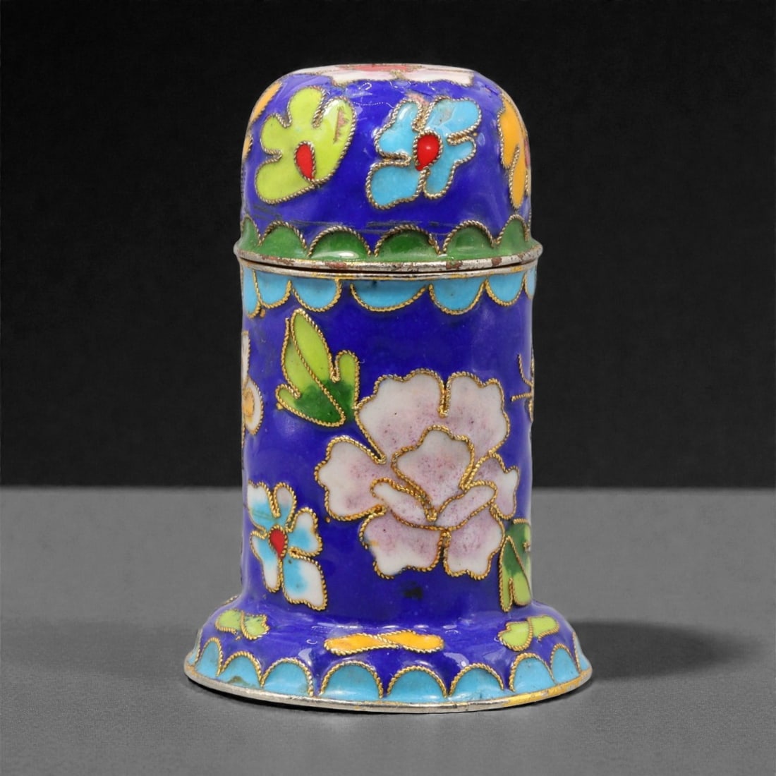 A Chinese Cloisonne Enamel Trinket Box, 20th Century, 84YC: The box is constructed of metal and decorated with cloisonne enamel, formed as a cylindrical vessel with a slightly flared base and a domed cover. The exterior is enameled on a deep blue ground with s