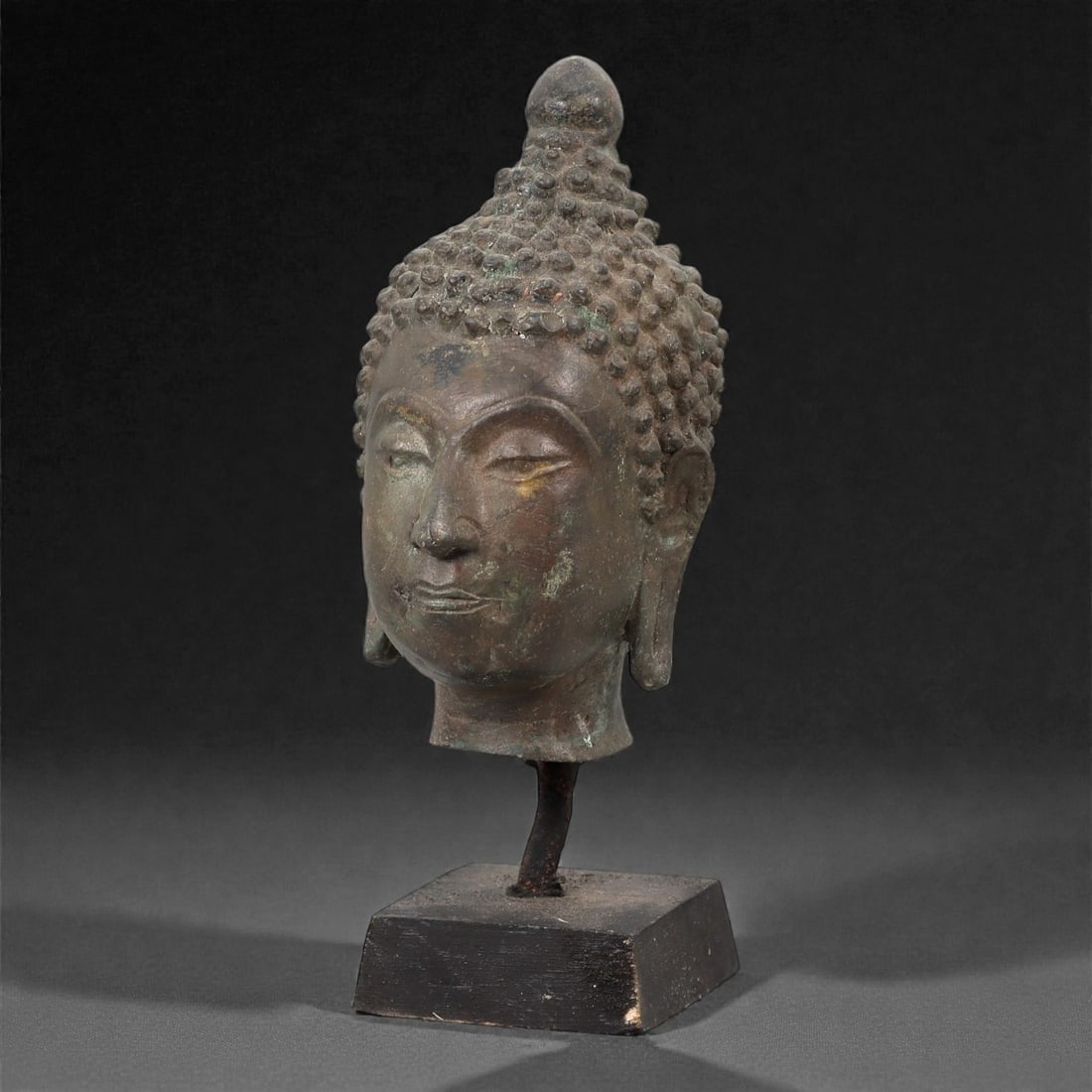 A Buddhist Bronze Head, 20th Century, 15FJ: Cast in bronze, the head depicts the Buddha with a calm, meditative expression, featuring downcast eyes, gently arched brows, and a softly modeled mouth. The hair is rendered as tightly arranged curls