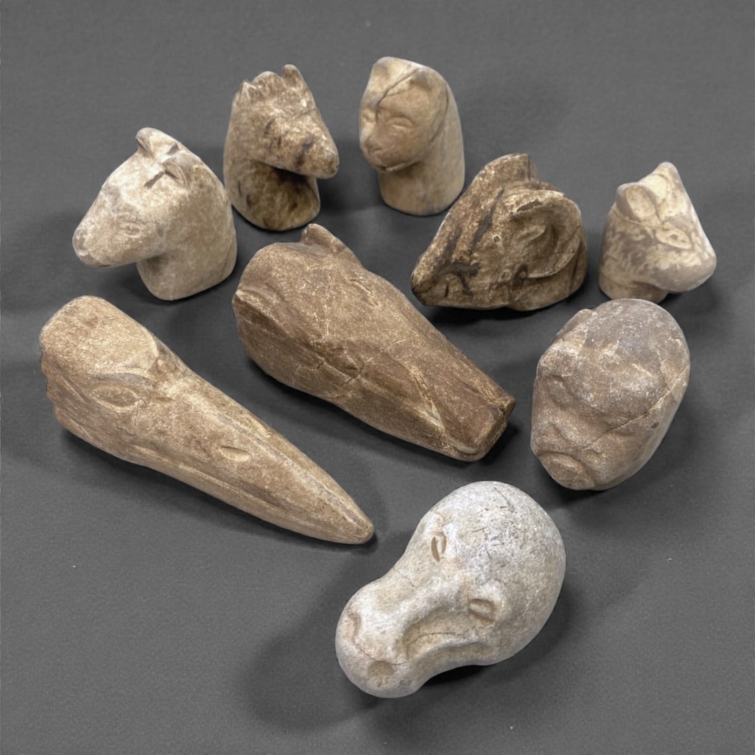 A Group of Near Eastern Stone Zoomorphic Figurines, Ancient Period, 73XJ: Comprising nine small stone figurines carved from light to dark-toned stone with natural veining and inclusions, the group represents stylized zoomorphic heads and animal forms rendered in the round,