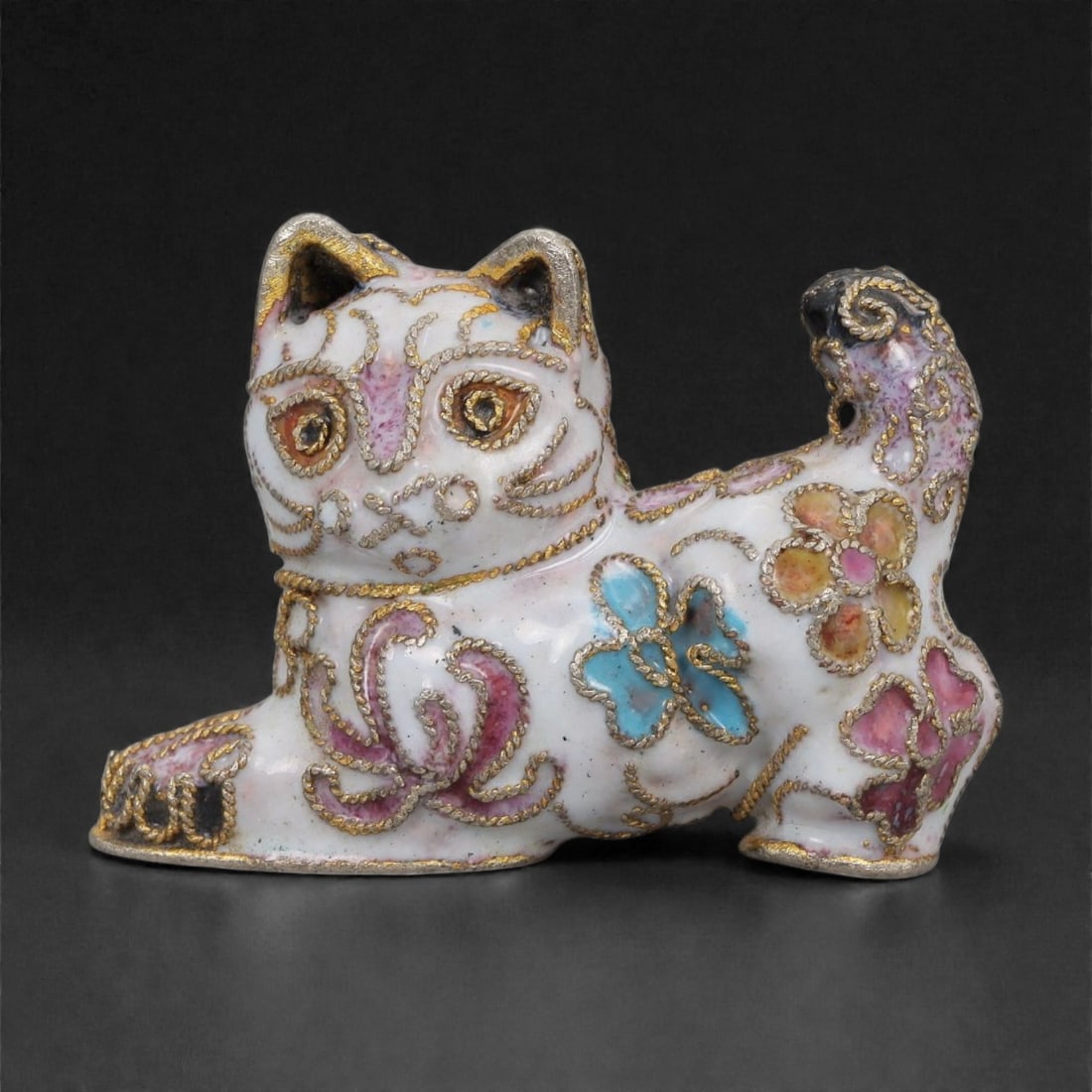 A Chinese Cloisonne Enamel Cat Effigy, 20th Century, 11FH: Modeled as a recumbent cat with the head raised and tail curled along the body, the effigy is constructed over a metal core and decorated overall with cloisonne enamel on a white ground, the surface a