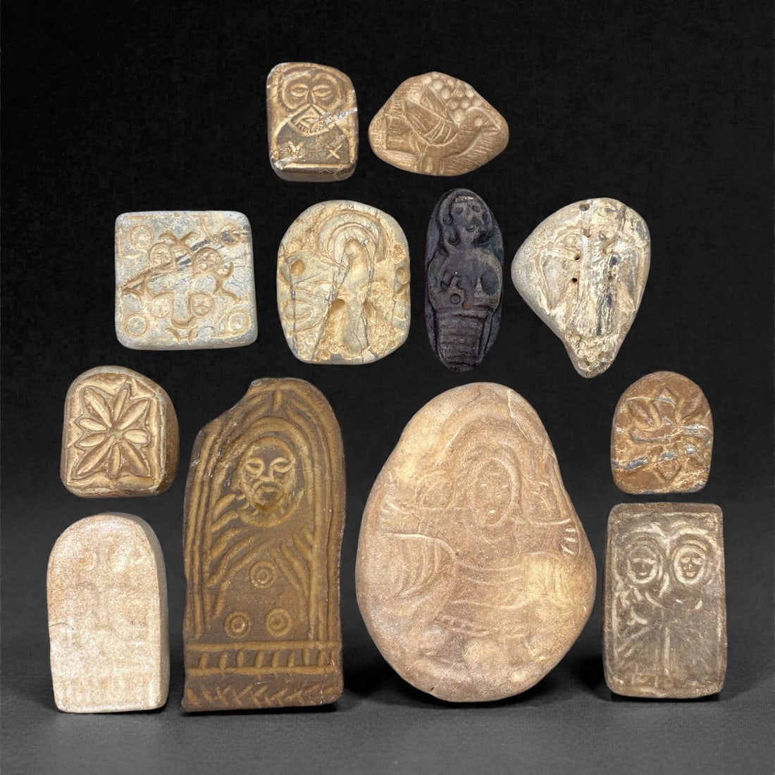 A Group of Medieval Christian Stone Devotional Objects, 12th-15th Century, 92W: Carved from light beige, buff, and darker brown stone with visible veining, inclusions, and areas of surface abrasion, the group comprises twelve small devotional plaques and reliefs executed in low r