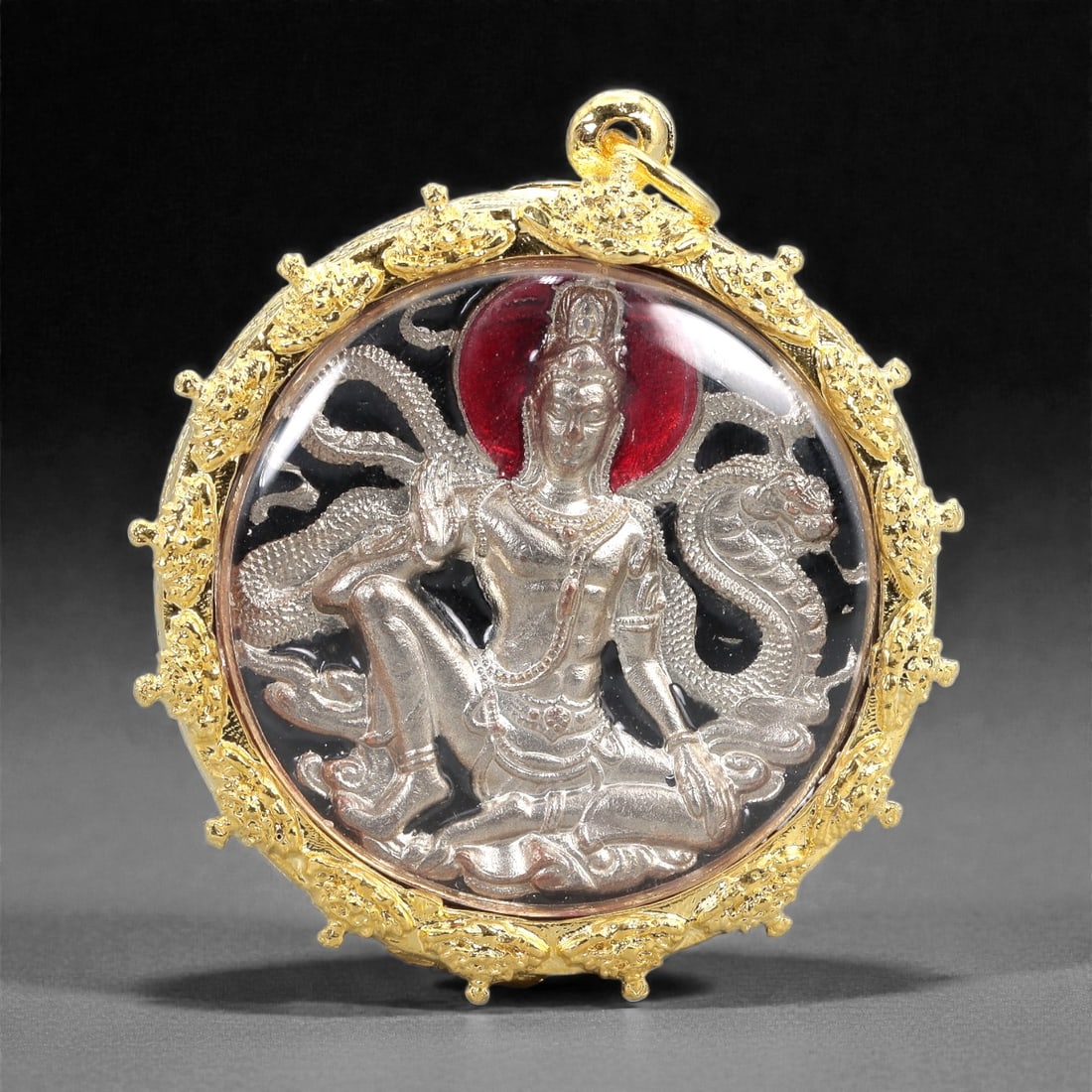 A Gilt-Framed Buddhist Deity Amulet, 20th Century, 22FJ: The amulet is centered on a finely cast silver-toned relief depicting a seated Buddhist deity or bodhisattva in a dynamic pose, shown with one leg raised and the other folded beneath, surrounded by a