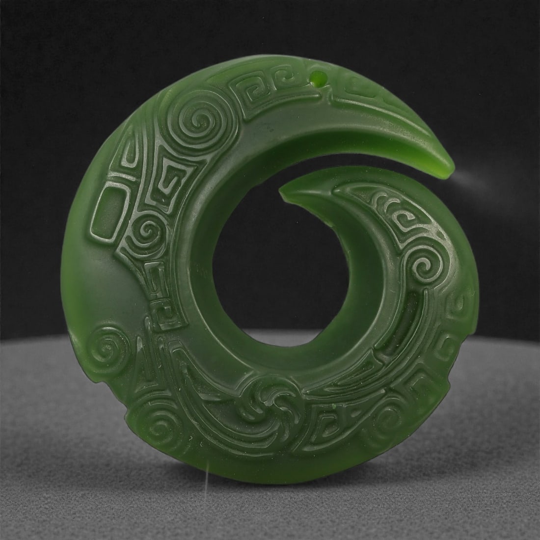 A Chinese Green Jade Openwork Disc, 20th Century, 91FD: Carved from translucent green jade with a uniform tone and a softly polished surface. The object is formed as an openwork disc with a continuous curved profile, interrupted by a crescent-shaped openin