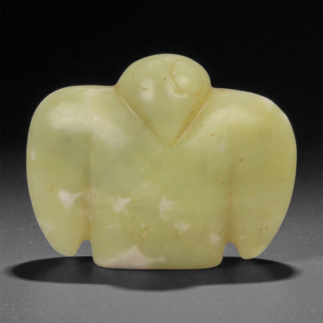 A Chinese Pale Yellow Jade Bird-Form Amulet, 20th Century, 41FD: Carved from pale yellow jade with soft translucency and scattered white inclusions, the object is worked as a stylized bird shown frontally with outspread wings. The head is centrally positioned, with