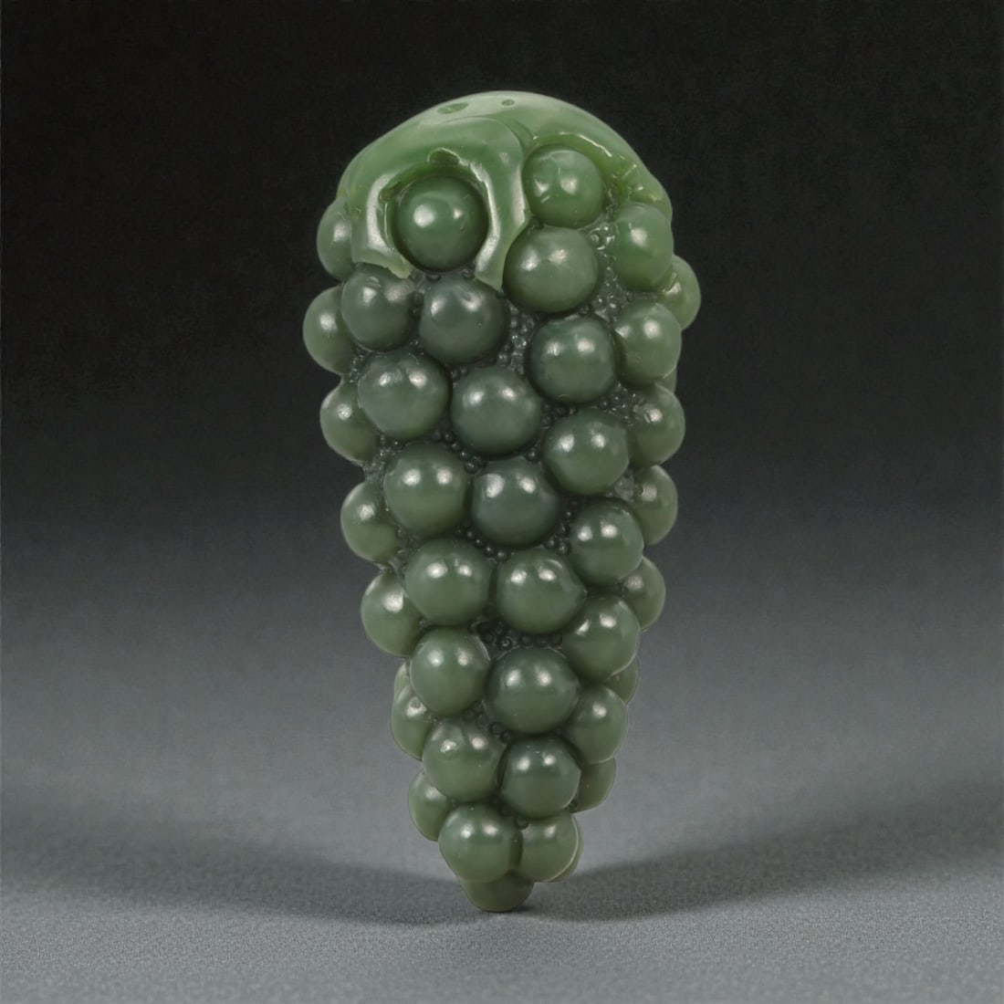 A Chinese Nephrite Jade Grape-Form Pendant, 20th Century, 6FC: Carved from dark green nephrite jade with even coloration and a high, glossy polish, the pendant is modeled in the form of a pendant cluster of grapes. The surface is worked in high relief with tightl