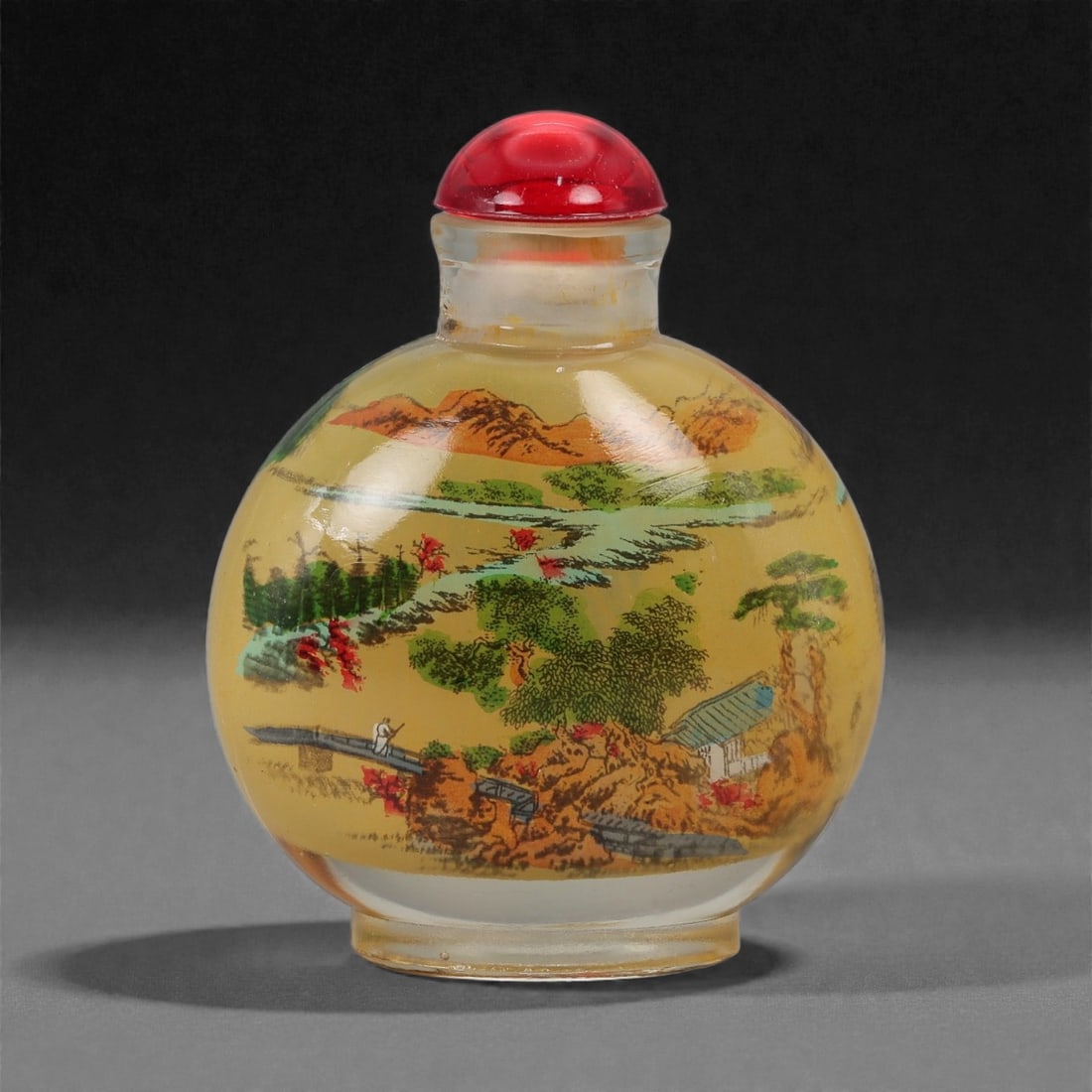 A Chinese Glass Snuff Bottle with Inside-Painted Landscape Scenes, 20th Century, 44FD: Formed from clear glass with a rounded flattened body, short cylindrical neck, and recessed oval foot, fitted with a domed red stopper. The interior is hand-painted in polychrome with continuous lands