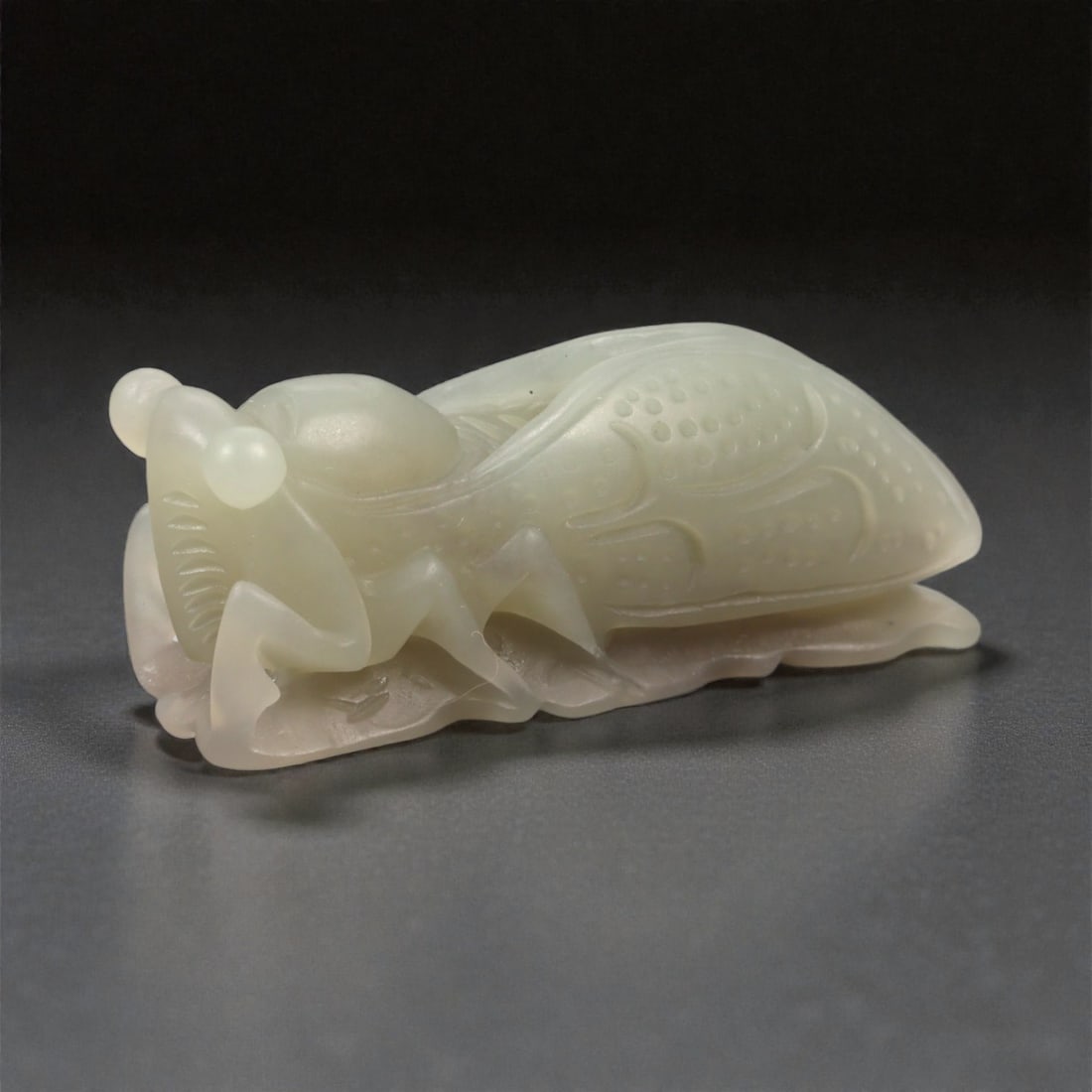A Chinese Nephrite Jade Cicada Figure, 20th Century, 7FB: Carved from pale celadon nephrite jade with soft translucency and minor natural inclusions, the figure represents a cicada shown in a recumbent posture with folded legs beneath the body. The wings are