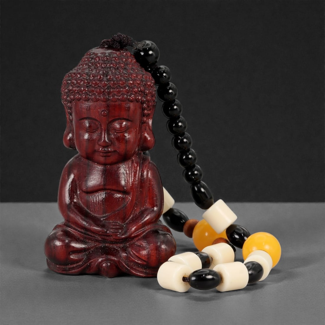 A Chinese Wood Figure of Buddha, 20th Century, 88FD: Carved from dark-toned wood with a polished surface, depicting a seated Buddha shown frontally with legs crossed and hands resting at the abdomen. The head is modeled with tightly curled hair and elon