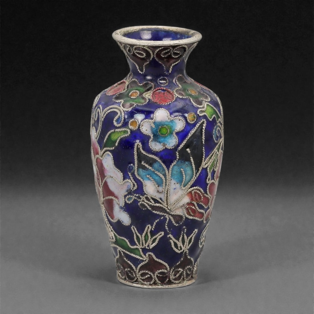A Chinese Cloisonne Enamel Vase, 20th Century, 98FG: Constructed from a copper alloy body and decorated with cloisonne enamel, the vessel is of small baluster form with a rounded shoulder, tapering lower body, and a flared neck terminating in a metal-ri