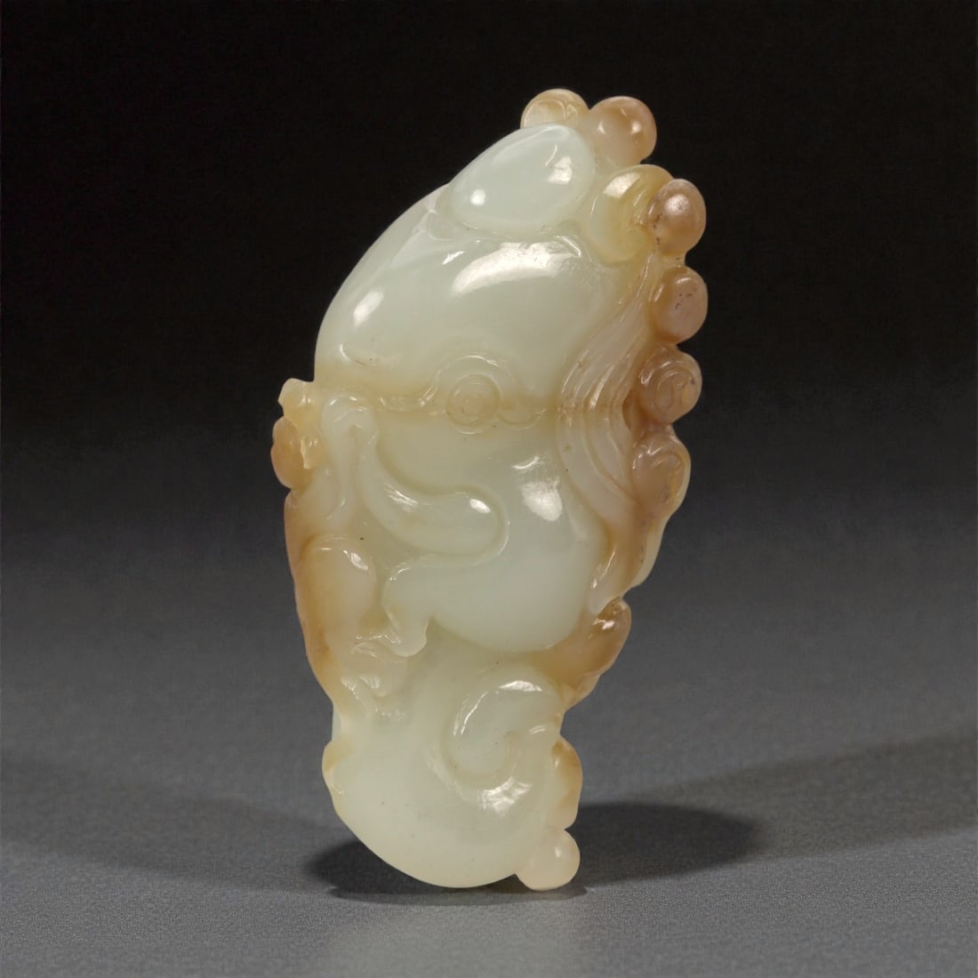 A Chinese Nephrite Jade Cloud-Form Pendant, 20th Century, 14FB: Carved from pale celadon Hetian nephrite jade with areas of retained russet skin, the pendant is worked in high relief in an abstract cloud-form composition. The carving is composed of layered, curlin