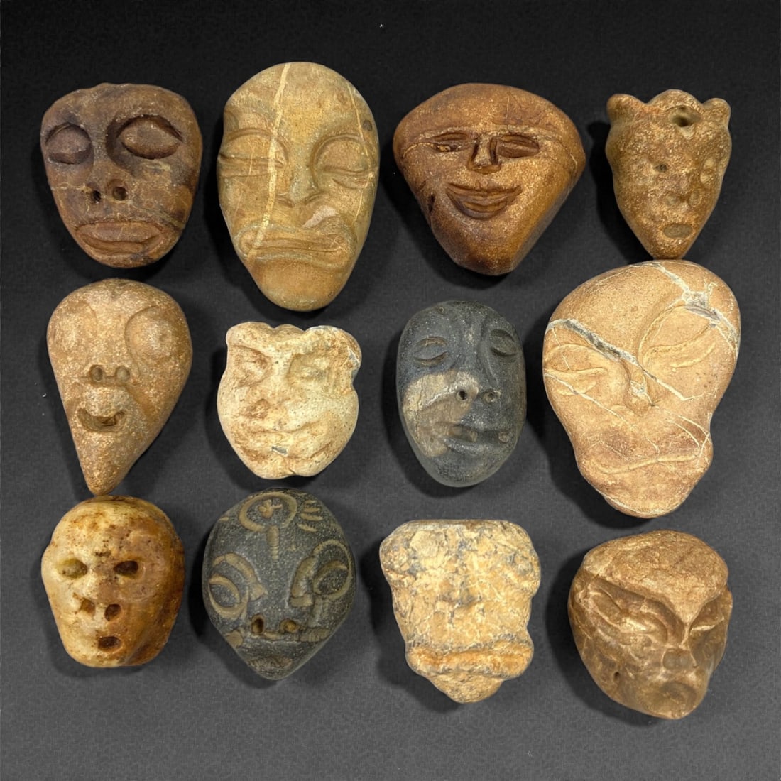 A Lot of Ancient Mediterranean Stone Maskettes, 12th-17th Century, 2.5-3.8cm, 49V: The group comprises lot of small maskettes carved from various stone types, including limestone and related sedimentary materials, displaying a range of natural tones from pale beige and ochre to dark
