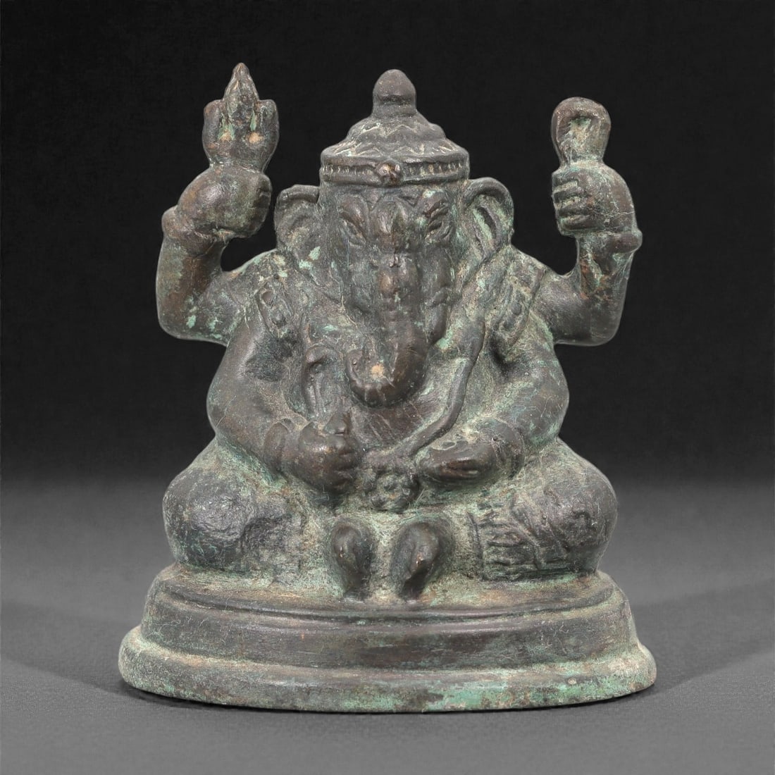 An Indo Himalayan Bronze Ganesha Figure, 20th Century, 16FJ: Cast in bronze, the figure represents Ganesha seated in a frontal pose on a low circular base. The elephant-headed deity is shown with a rounded torso and multiple arms, the upper hands raised and hol