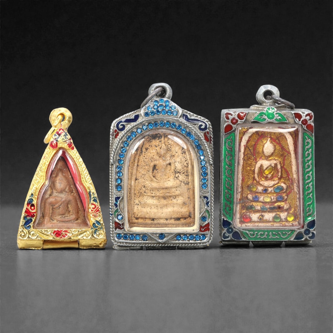 A Group of Thai Clay and Composite Buddhist Amulets, 20th Century, 19ZG: Comprising three molded Buddhist amulets formed from pale buff and reddish-brown clay and composite materials, each depicting a seated Buddha in meditation posture upon a stepped base. The figures are