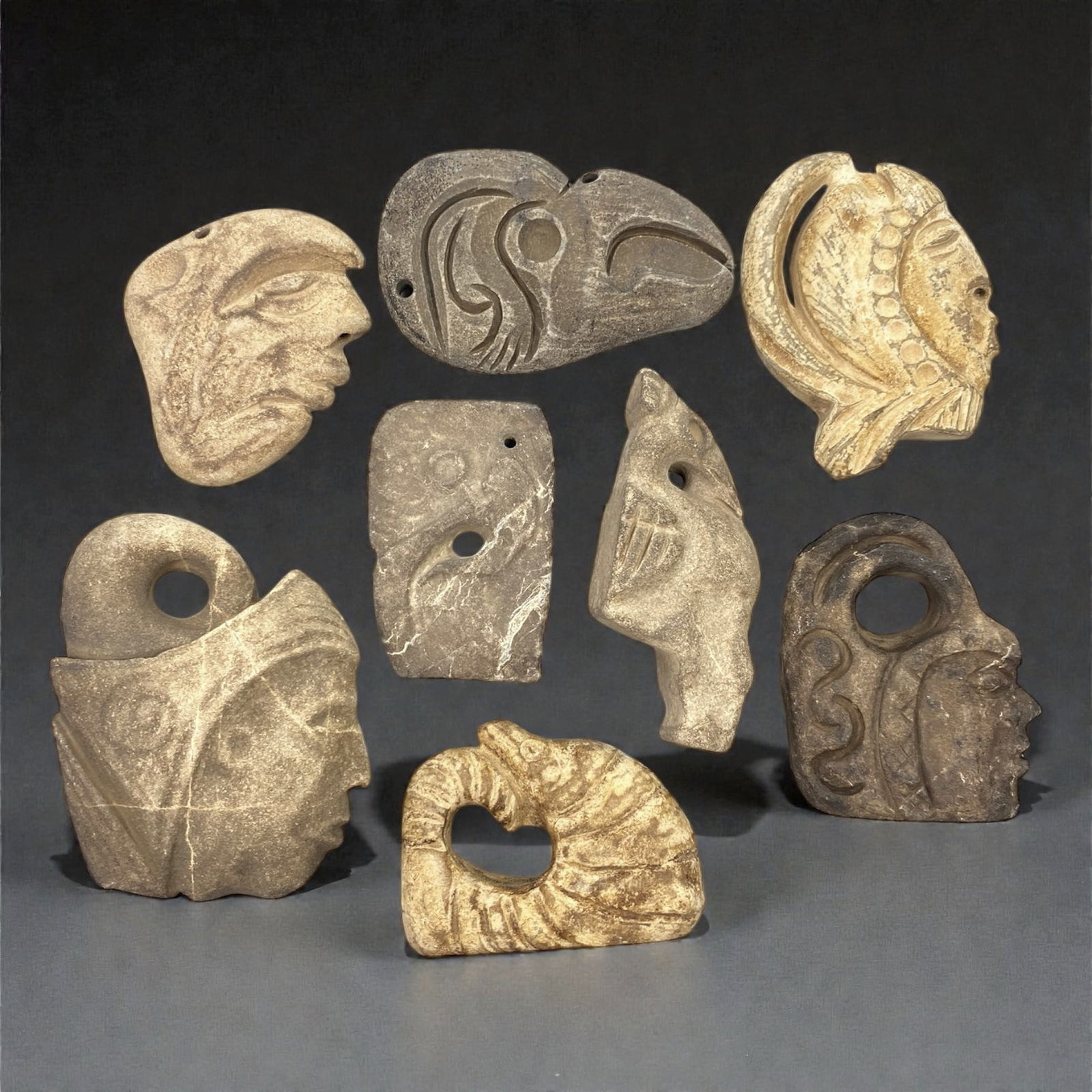 A Group of Mesoamerican Stone Sculptural Pendants, Pre-Columbian Period, 59XJ: The group comprises eight small stone sculptural pendants carved from light and dark-toned stone, including volcanic and sedimentary materials. The objects are worked in relief and low sculptural mode