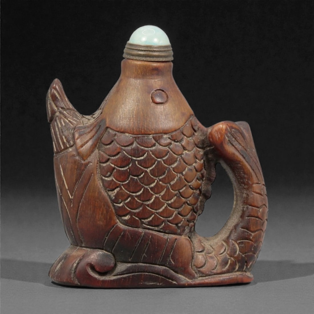 A Chinese Wood Fish-Form Snuff Bottle, 20th Century, 7YC: Carved from hardwood with a warm brown tone and visible grain, the bottle is formed as a stylized fish shown in profile, with the body hollowed from the mouth to accommodate snuff. The surface is carv