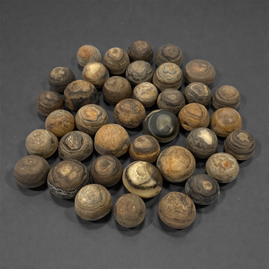 A Group of Tibetan Luk Mik ("Goat's Eye") Agate Beads, 19th-20th Century, 43W: Comprising thirty-eight spherical and near-spherical beads carved from agate, the group is distinguished by concentric banding and circular "eye" formations characteristic of Luk Mik ("goat's eye") be