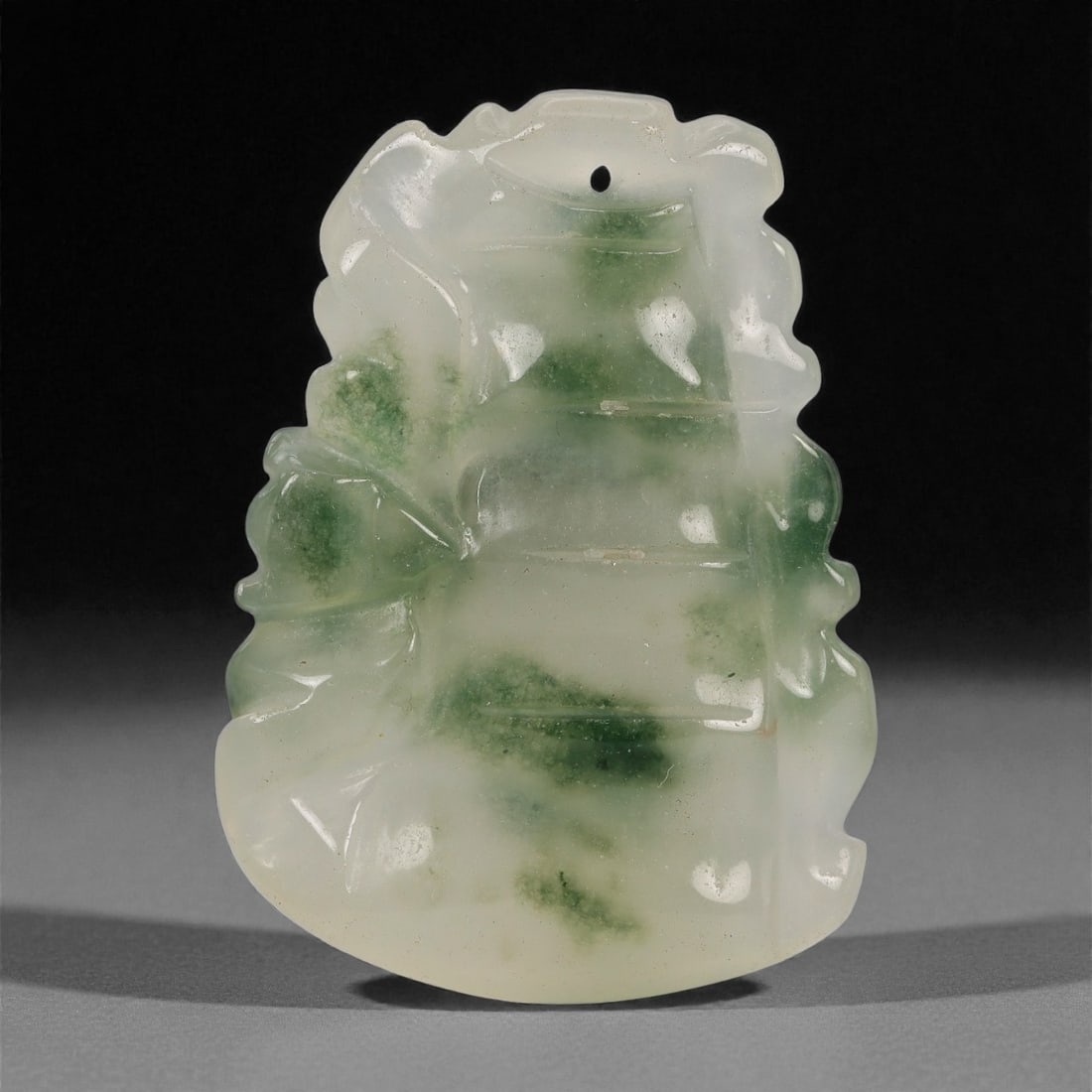 A Chinese Mottled Jade Pendant, 20th Century, 97FD: Carved from translucent pale green and white jade with darker green inclusions, worked in low relief and polished overall. The pendant is formed as a vertically tiered motif with projecting scroll and