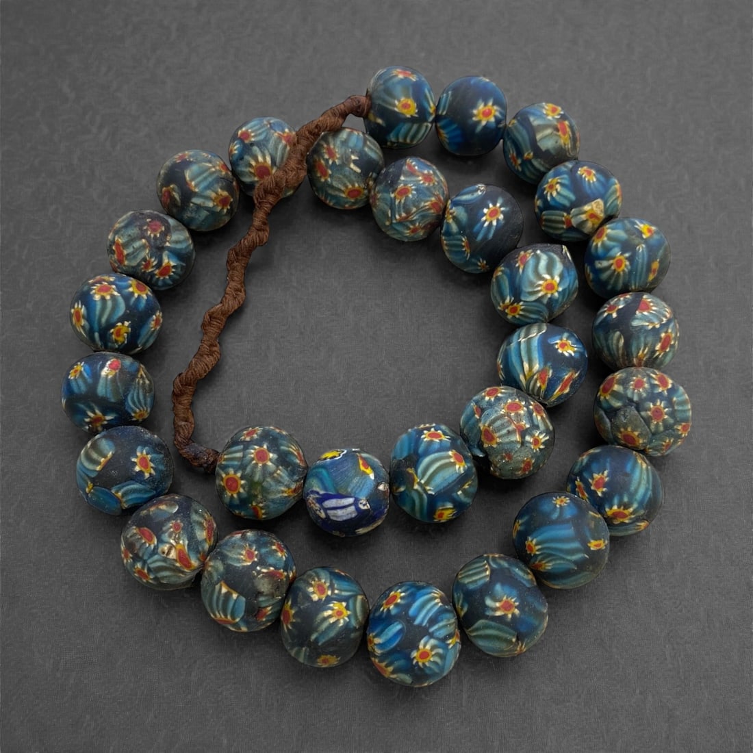 A Venetian Glass Millefiori Bead Necklace Strand, 19th Century, 390g, 4AA: Composed of spherical glass beads decorated with millefiori canes, featuring a dark blue ground with radiating patterns of yellow, red, and white, strung on a modern braided fiber cord. The intricate