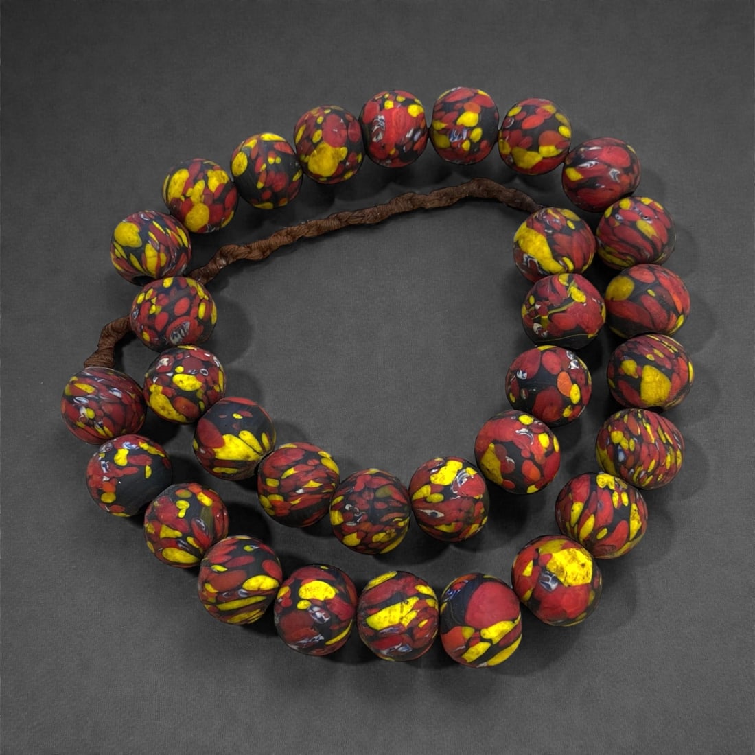 A West African Glass Mosaic Bead Necklace Strand, 19th-Early 20th Century, 290g, 7AA: Composed of spherical glass beads with a matte black ground decorated with irregular patches of bright red and yellow, strung on a modern braided fiber cord. The mosaic pattern is characteristic of We