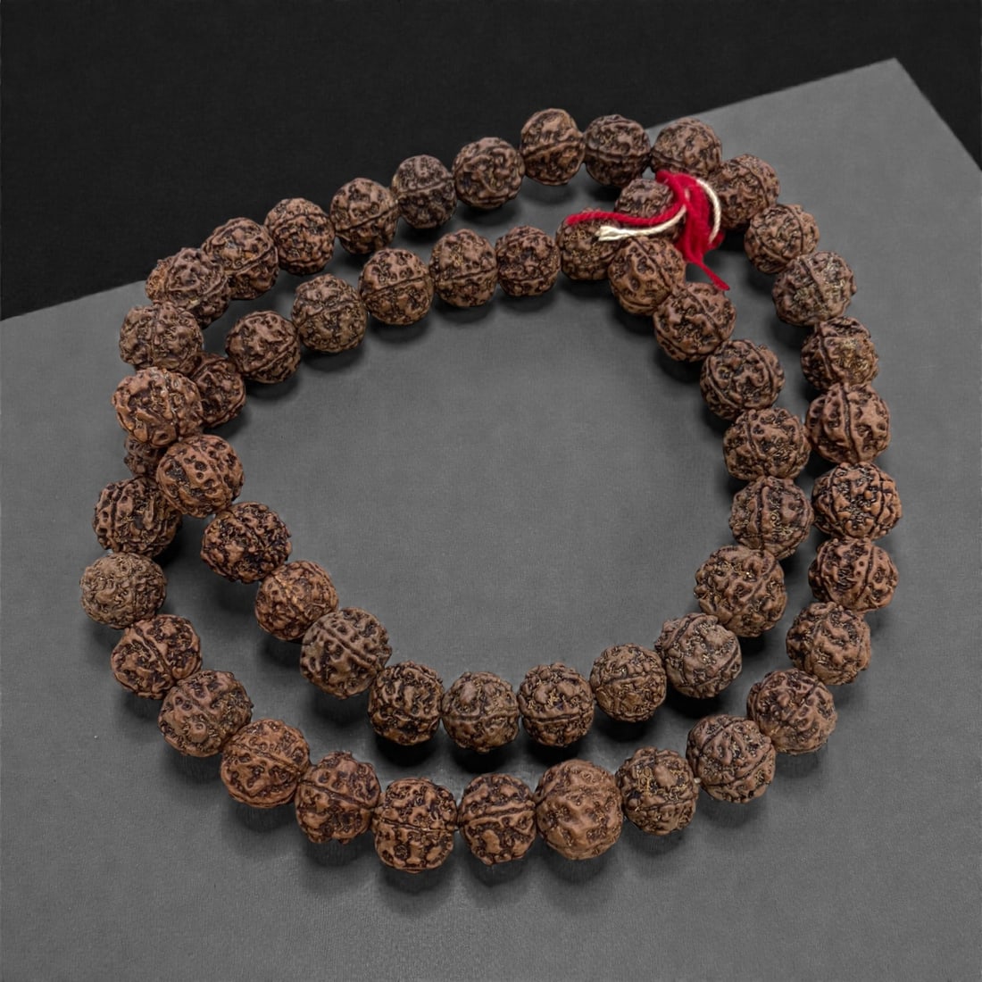 An Antique Indian Rudraksha Seed Bead Mala, 19th Century, 131g, 27AA: Composed of natural rudraksha seeds, strung with red cotton thread separators and finished with a traditional red tassel. Rudraksha seeds are sacred in Hindu and Buddhist traditions, believed to posse