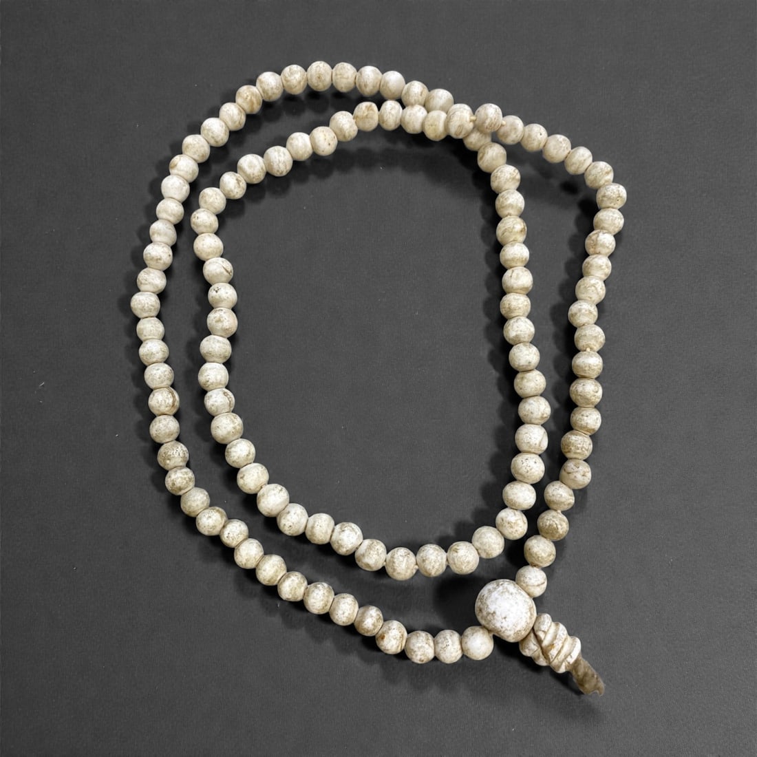 An Antique Tibetan Conch Shell Bead Mala, 19th Century, 115g, 32AA: Composed of spherical conch shell beads, strung with a traditional guru bead and tassel terminal, in an aged off-white patina. Conch shell is sacred in Tibetan Buddhism, symbolizing the sound of the D