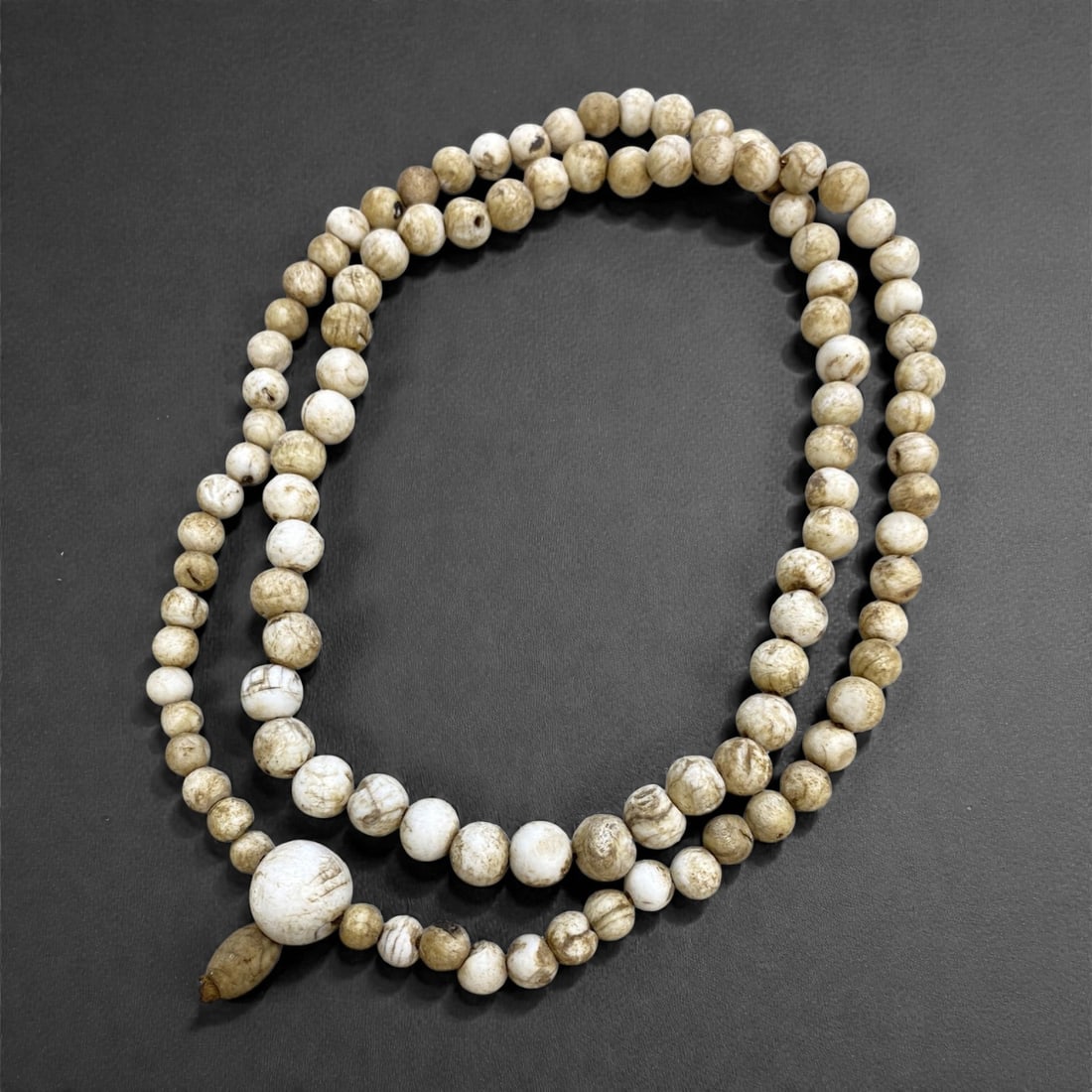 An Antique Tibetan Conch Shell Bead Mala, 19th Century, 161g, 36AA: Composed of spherical conch shell beads, strung with a traditional guru bead and tassel terminal, in an aged off-white patina. Conch shell is sacred in Tibetan Buddhism, symbolizing the sound of the D