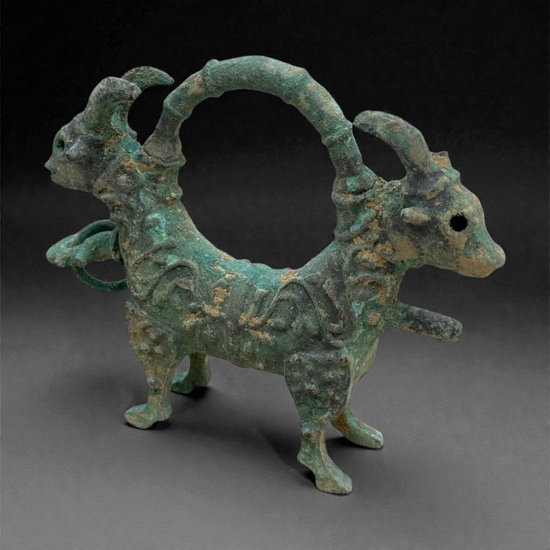 A Byzantine Bronze Lock, 10th-12th Century, 158g, 46AA: Cast from bronze with a textured surface and green patina with areas of light brown encrustation, the lock is formed as a zoomorphic double-headed creature, likely ibex or goat, with a continuous arch
