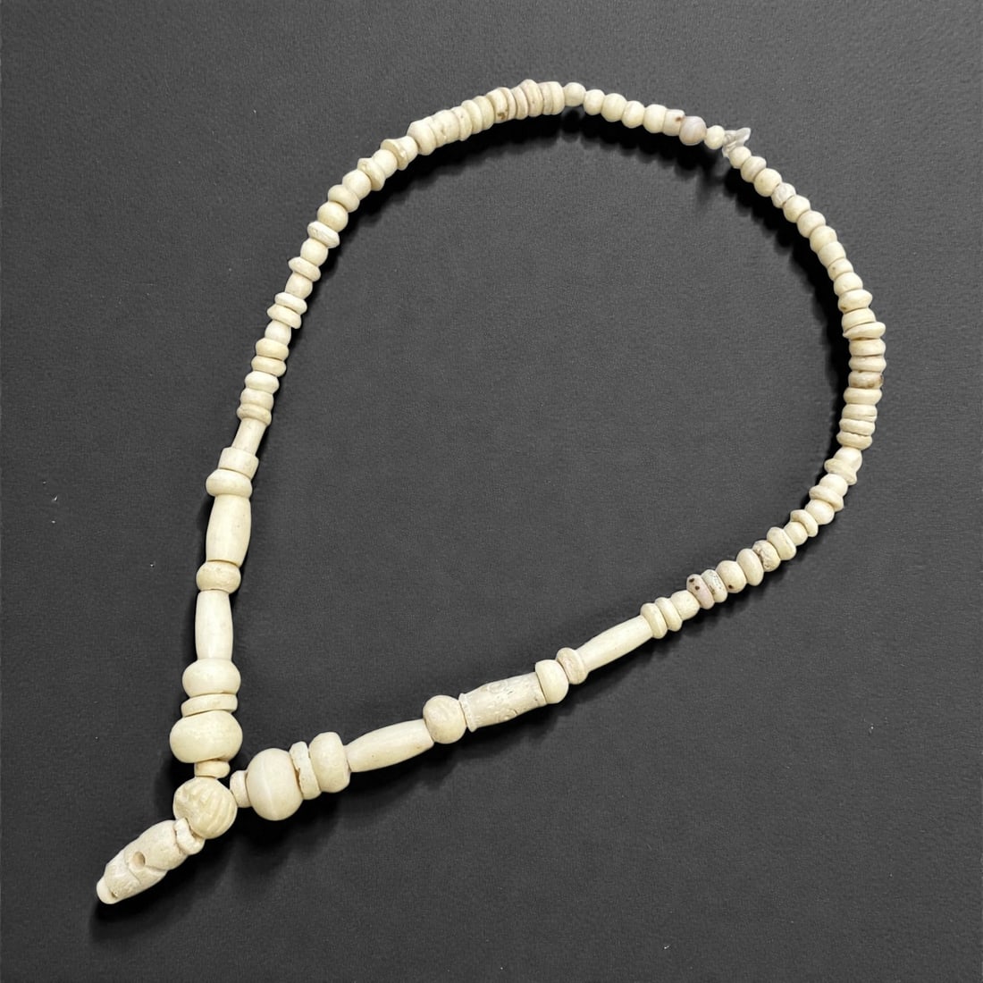 A Near Eastern Bone Bead Necklace Strand, 3rd-2nd Millennium BCE, 15g, 49AA: Composed of bone beads, the strand features a graduated sequence of forms: small, flattened disc beads, short cylindrical beads, and larger, rounded barrel beads, with a pointed terminal bead at one e