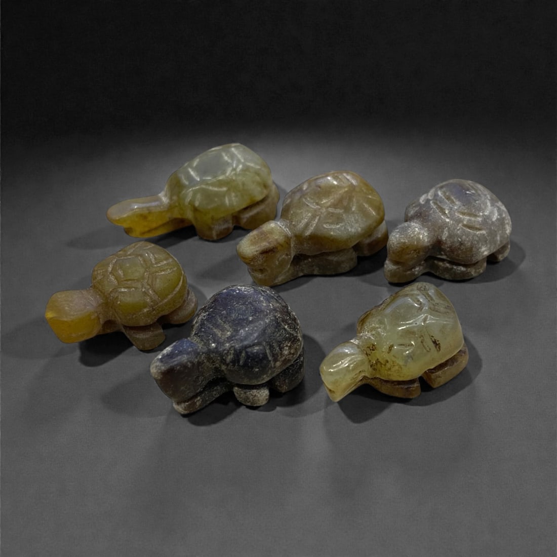 A Group of Six Chinese Jade Tortoise Figures, 21g, 83AA: Comprising six carved jade tortoise figures. The jade exhibits a range of hues, including pale green, yellowish-green, and dark brown, with natural tonal variations and subtle surface patination. Each