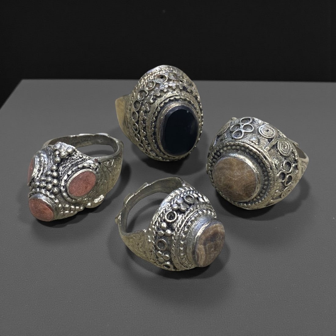 A Group of Four Antique Silvered Bronze Rings, 19th Century, Size 8.5US, 61g, 62AA: Each ring is crafted from silvered bronze, featuring ornate metalwork including filigree, repousse, and granulation details. The bezels are set with composite stones, the surfaces exhibit minor patina