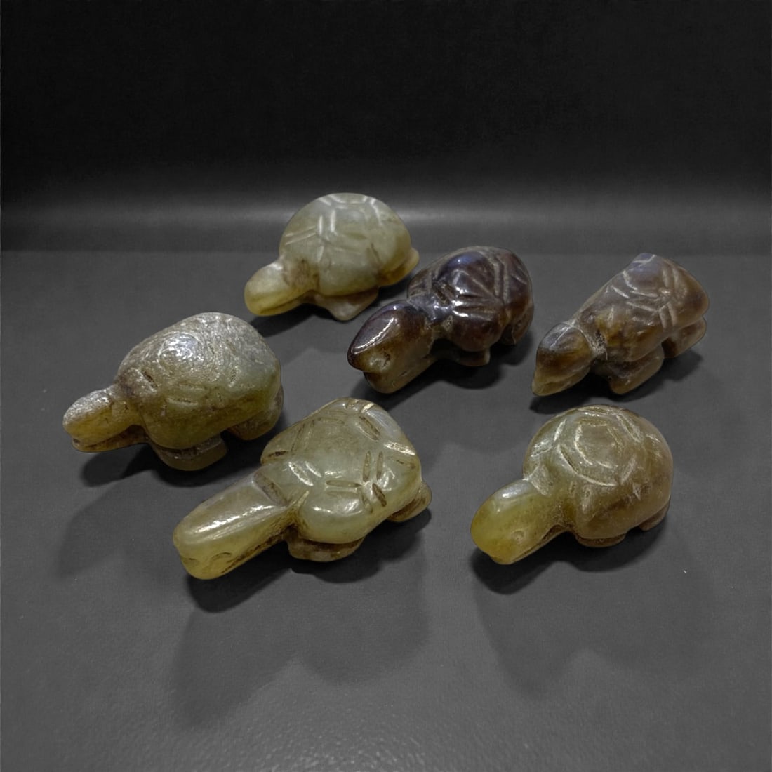 A Group of Six Chinese Jade Tortoise Figures, 17g, 82AA: Comprising six carved jade tortoise figures. The jade exhibits a range of hues, including pale green, yellowish-green, and dark brown, with natural tonal variations and subtle surface patination. Each