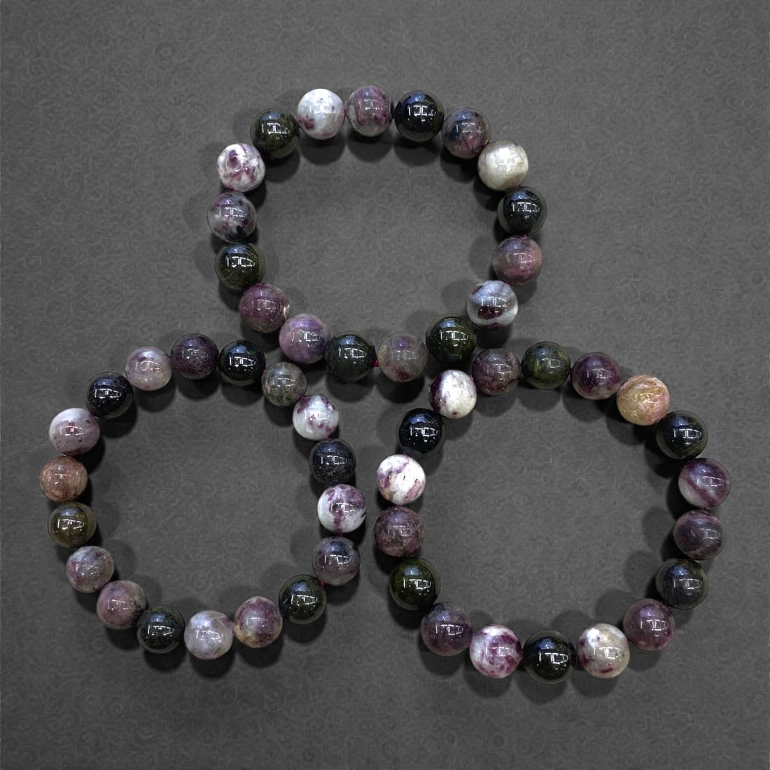 A Group of Three Tourmaline Beaded Bracelets, 130g, 72AA: Each bracelet is composed of polished round tourmaline beads, exhibiting a natural palette of pink, purple, green, and white with subtle matrix inclusions. The beads are strung on elastic cord for fle
